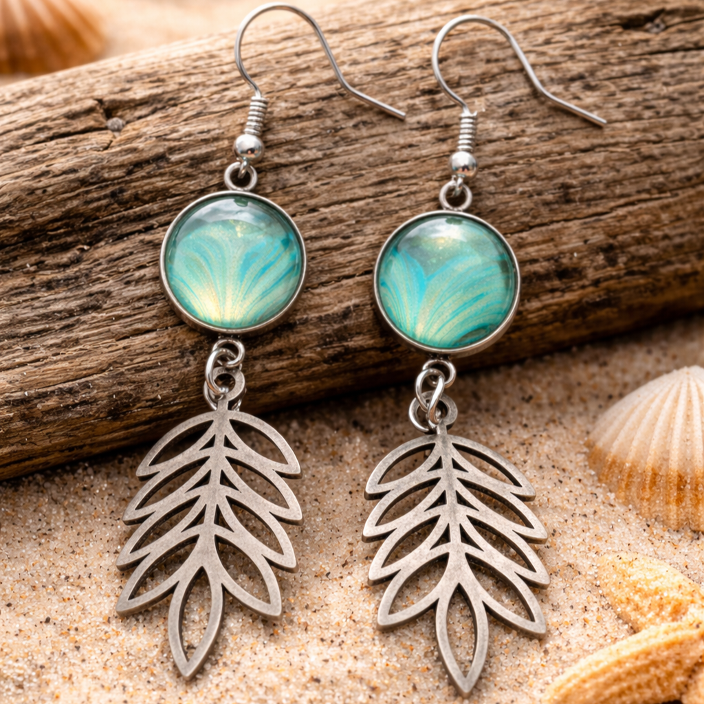 Pair of earrings with leaf-like designs on a wooden and sandy background